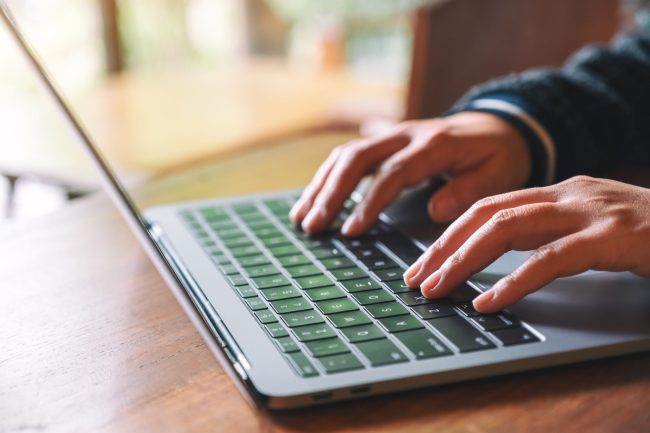 Closeup image of hands using and typing on laptop computer keyboard on the table